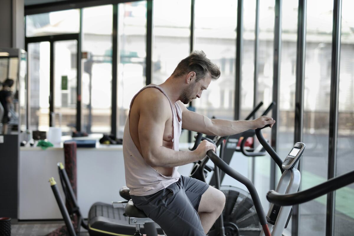 A man in a sleeveless shirt working out on an exercise bike.