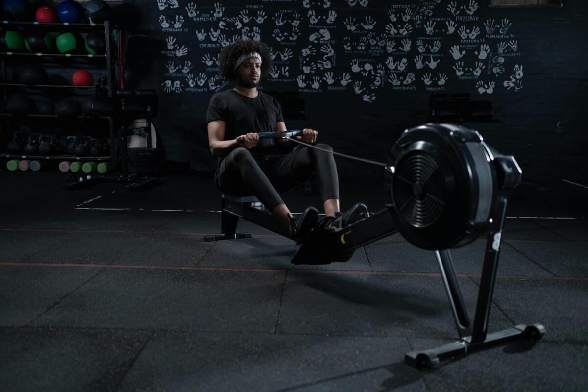 A man in a black shirt doing cardio exercises on a rowing machine.